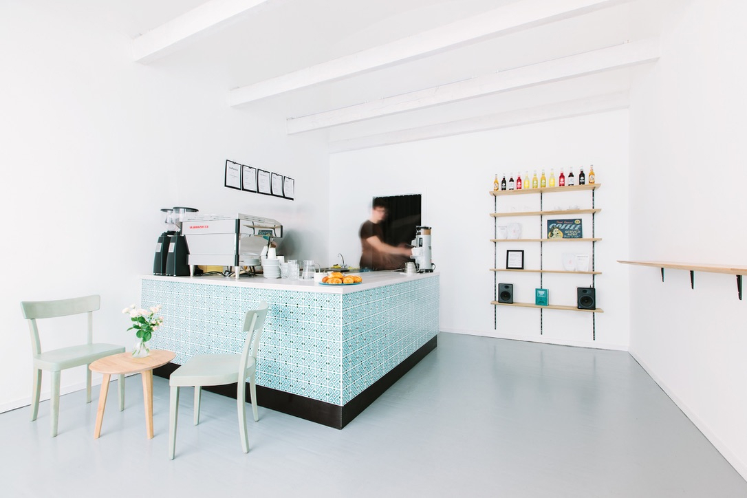 Photo of the café, indoors, with a barista behind the bar grinding coffee.